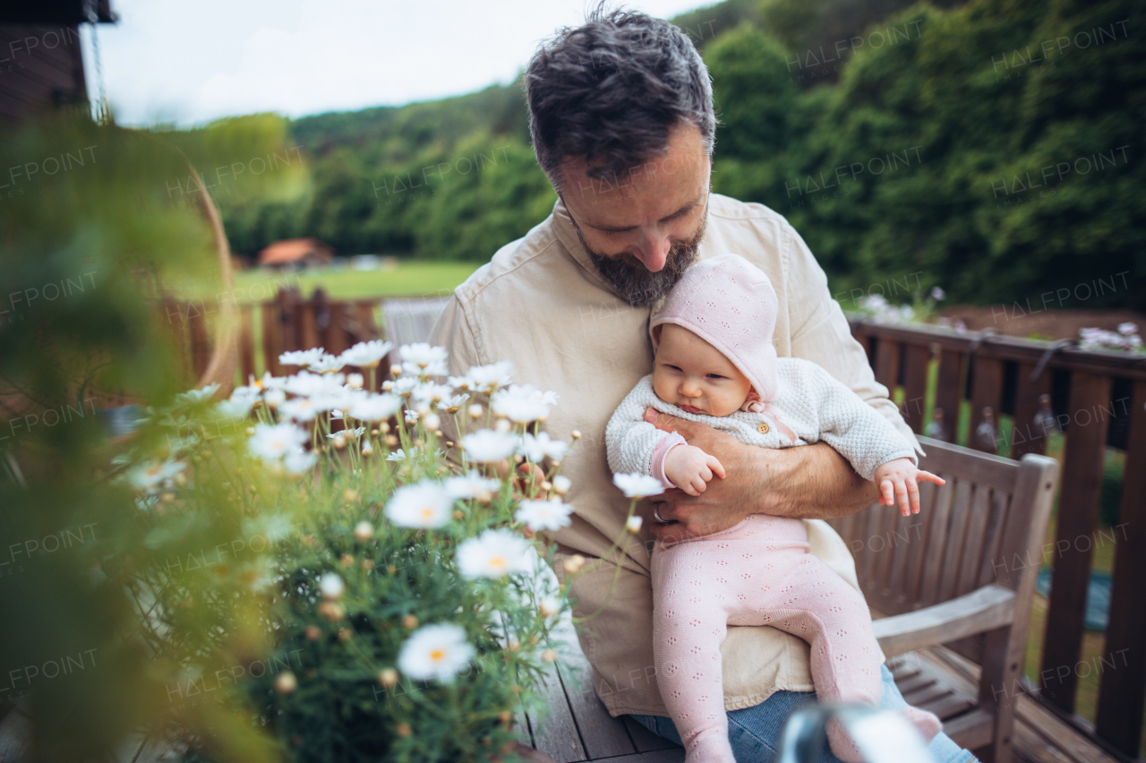 Father holding cute baby in arms, sitting on wooden patio and enjoying beautiful weater with baby daughter. Father's Day.