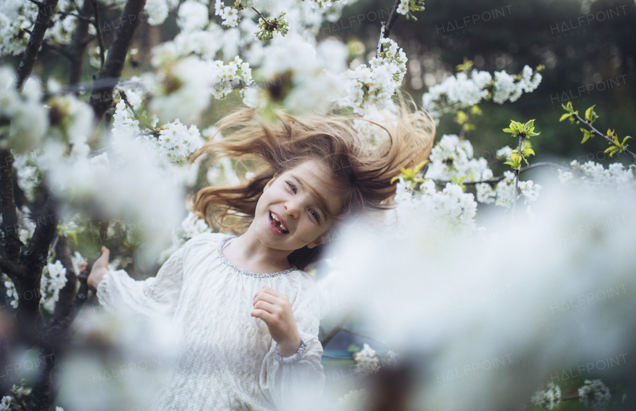 Laughing young girl dancing in the middle of blooming flowers. Concept of springtime in a nature.