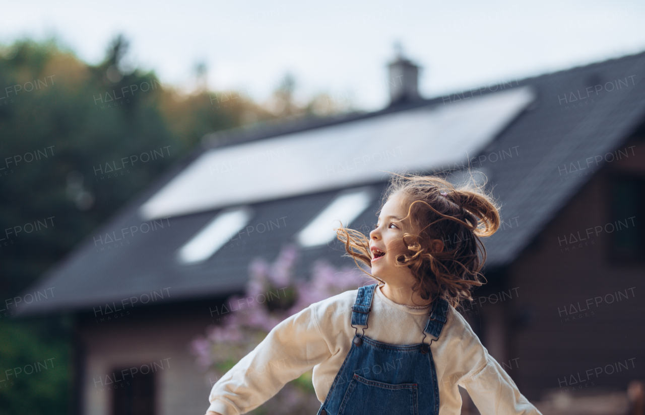 Beautiful young girl having fun outdoors. House with solar panels in background. Concept of springtime and solar energy.