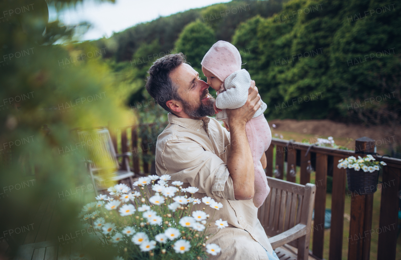 Father holding cute baby girl in arms, enjoying spring weater on patio. Father's Day concept.