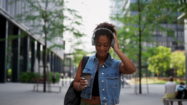 A Young woman walking through the city with backpack on back. University student is heading to class, holding a coffee in a travel cup.