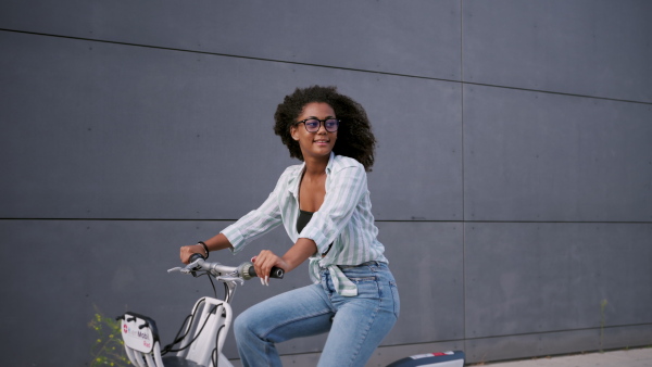 A beautiful university student is commuting through the city by bike, heading to class. Woman renting a city bike, using bike-sharing service.