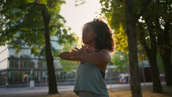 A young sporty woman exercising in city park, sitting on grass and stretching. Doing yoga outdoors at morning.