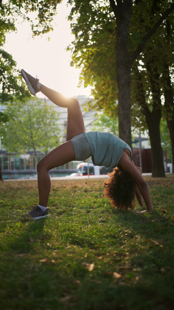 A young sporty woman exercising in city park, doing bridge pose or setu bandhasana in the park. Doing yoga outdoors at morning.