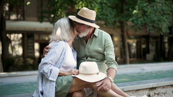 A senior couple enjoying hot summer in the city, sitting by the fountain, looking at each other. Staycation concept.