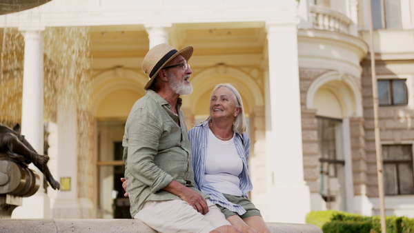 A senior couple enjoying hot summer in the city, sitting by the fountain, looking at each other. Staycation concept.