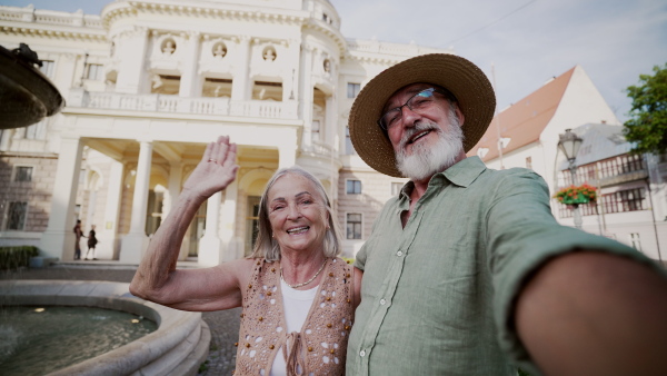 A senior couple taking selfie. Pensioners enjoying hot summer in the city, sightseeing, taking walk in historic part of city. Staycation concept.