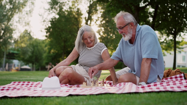 Elderly couple in love having a picnic in the city park, sitting on a picnic blanket, talking. Staycation concept.