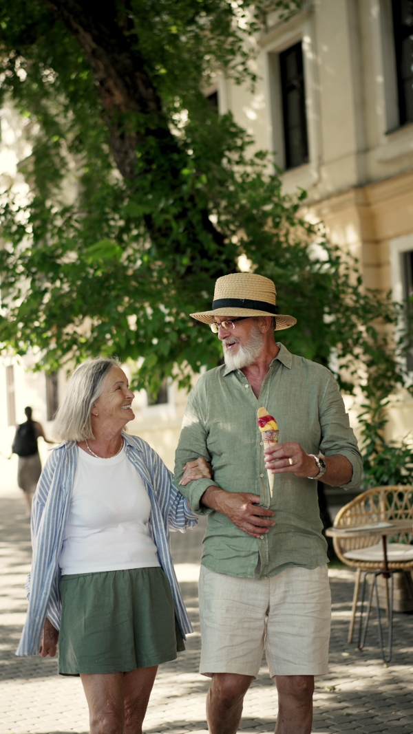 A senior couple enjoying hot summer in the city, eating ice cream while walking in historic part of city. Staycation concept.