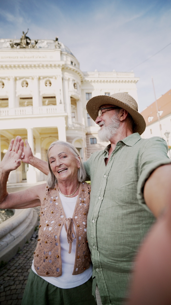 A senior couple taking selfie. Pensioners enjoying hot summer in the city, sightseeing, taking walk in historic part of city. Staycation concept.