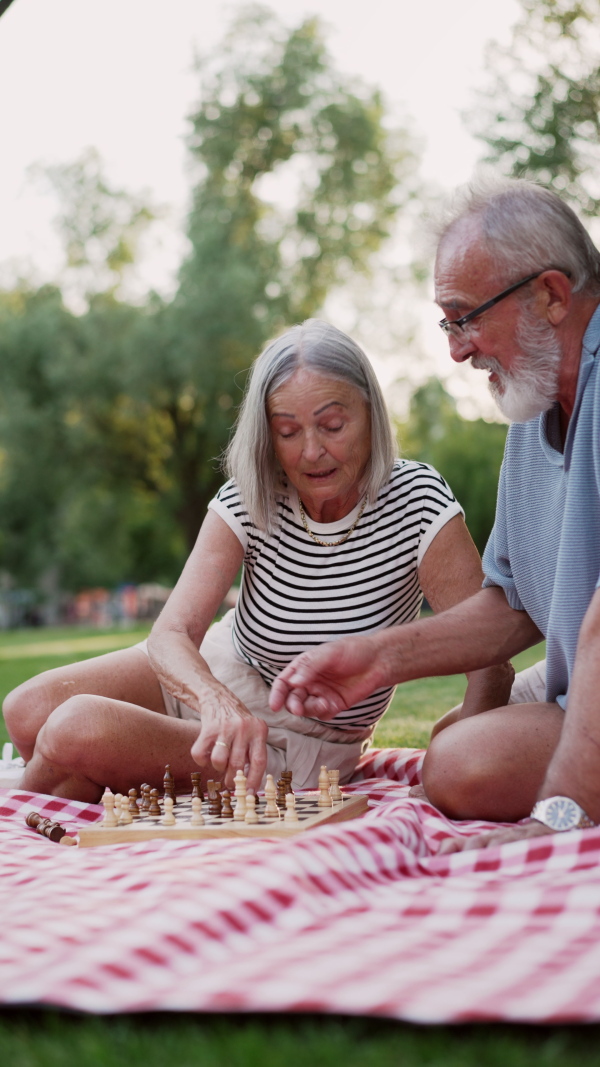 Elderly couple in love having a picnic in the city park, sitting on a picnic blanket, talking. Staycation concept.