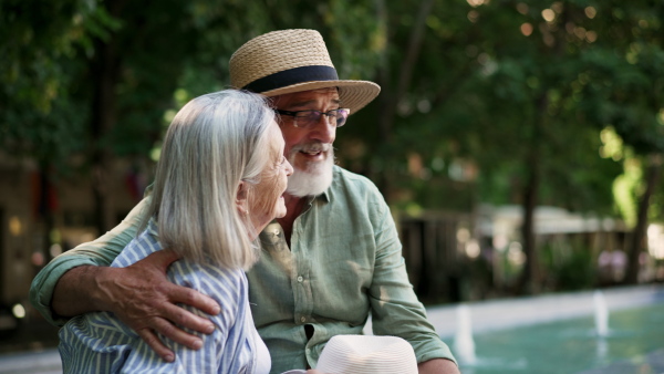 A senior couple enjoying hot summer in the city, sitting by the fountain, looking at each other. Staycation concept.