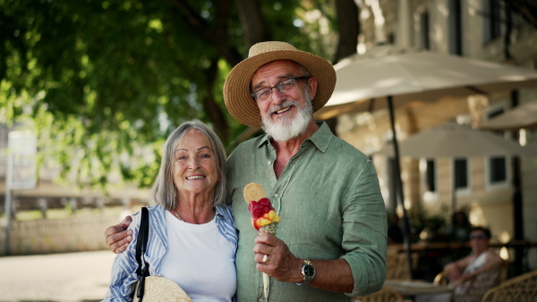 A senior couple enjoying hot summer in the city, eating ice cream while walking in historic part of city. Staycation concept.