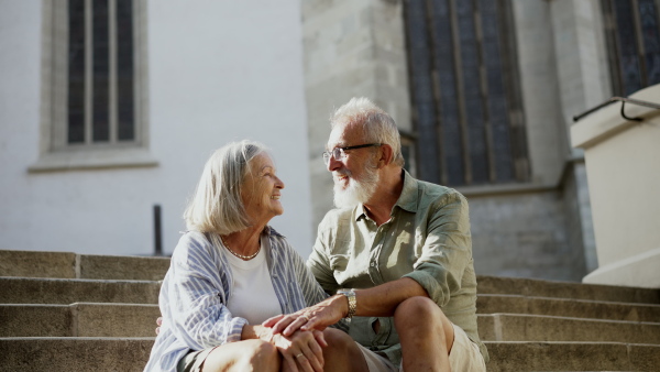 A senior couple enjoying hot summer in the city, sitting on historical staircase, looking at each other lovingly. Staycation concept.