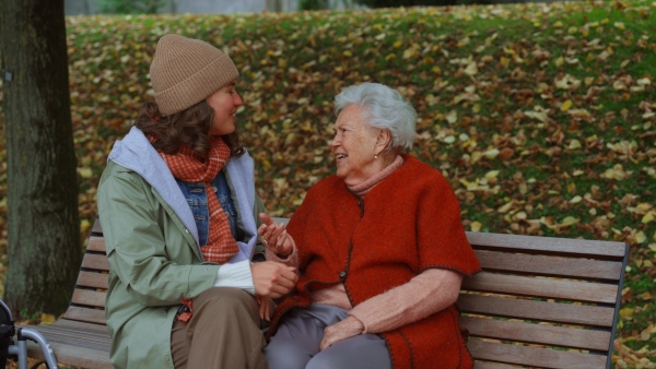 A video of granddaughter on an autumn walk in the park with her grandmother, sitting on bench and talking.