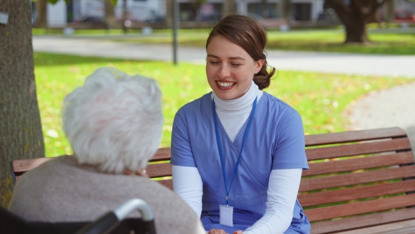 Disabled elderly woman in wheelchair talking with nurse, sharing her problems with female caregiver.