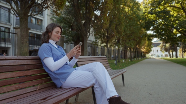 Beautiful nurse in uniform holding smartphone in hands, scrolling, looking at device screen