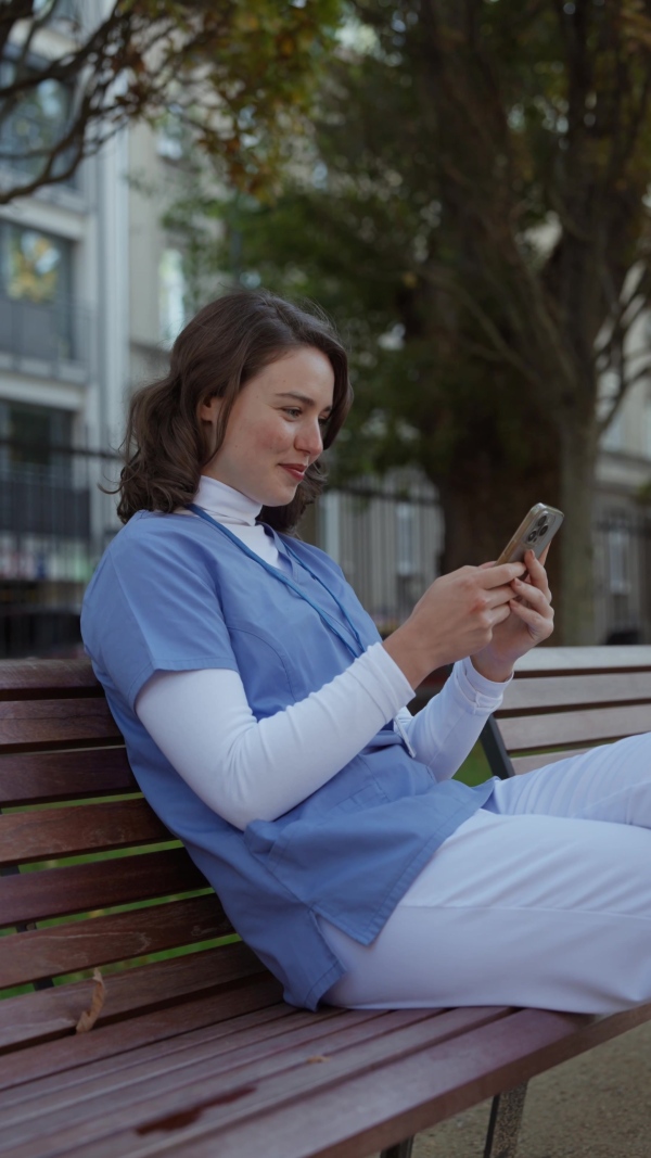 Beautiful nurse in uniform holding smartphone in hands, scrolling, looking at device screen