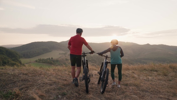 A senior couple on bike ride in autumn nature, enjoying beautiful view from hill. Older active people on electric bikes.