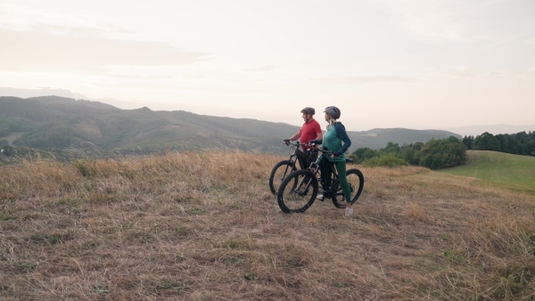 A senior couple on bike ride in autumn nature, enjoying beautiful view from hill. Older active people on electric bikes.