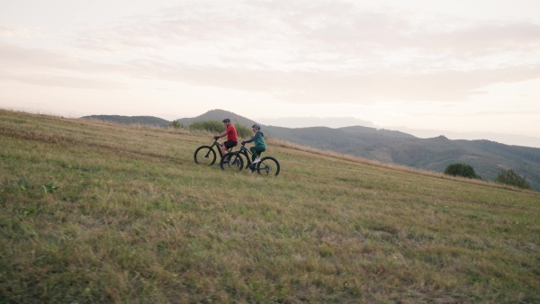 A senior couple on bike ride in autumn nature, enjoying beautiful landscape. Older active people on electric bikes.