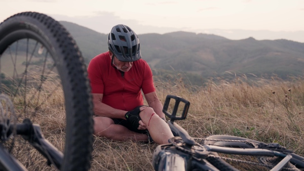 Elderly cyclist fell off his electric bike and has a bloody wound on his knee. The senior man examining his injured leg.