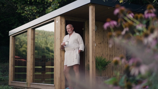 Handsome older man relaxing after spa session in home sauna, drinking herbal tea. Concept of hygge and slow life for senior people.