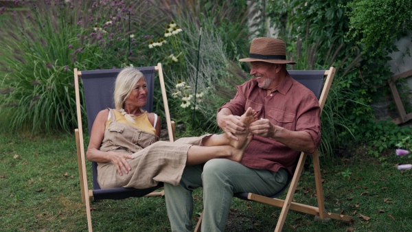 Handsome husband massaging wifes feet, enjoying peaceful moment in the garden. Concept of hygge and slow life for senior people.