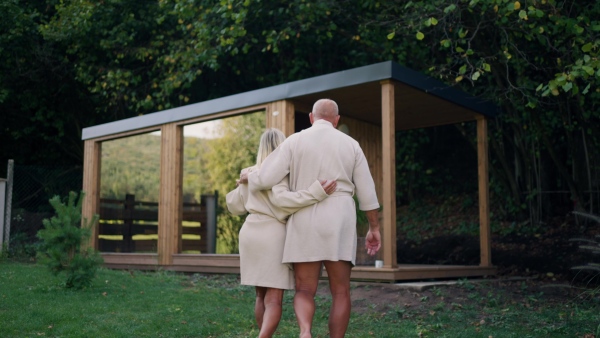 Older couple in love wearing bathrobe, getting ready to go into home sauna. Concept of hygge and slow life for senior people.