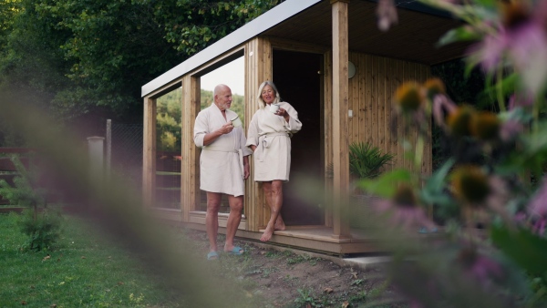 Husband and wife relaxing after spa session in home sauna, drinking herbal tea. Concept of hygge and slow life for senior people. Banner with copy space.