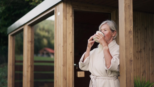 Beautiful older woman relaxing after spa session in home sauna, drinking herbal tea. Concept of hygge and slow life for senior people.