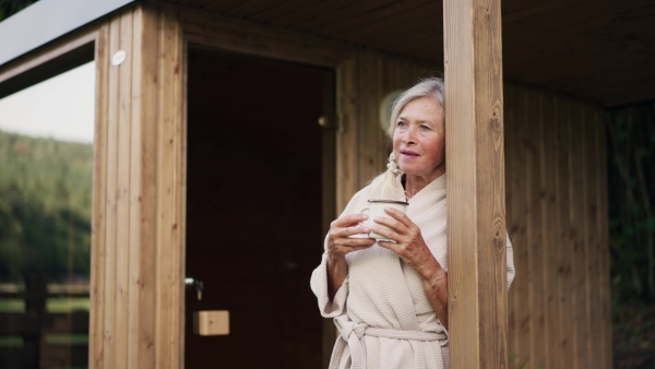 Beautiful older woman relaxing after spa session in home sauna, drinking herbal tea. Concept of hygge and slow life for senior people.