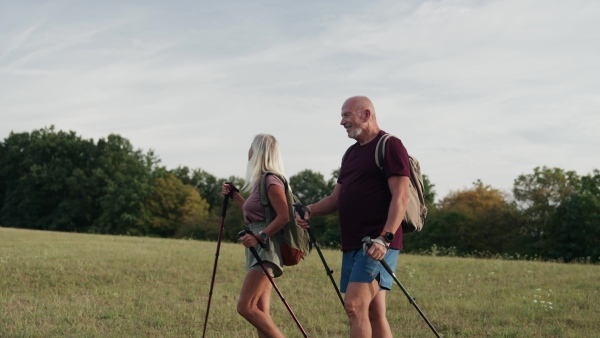 Active senior couple spending their free time outdoors, hiking in nature. Senior man and woman with trekking poles and backpack.