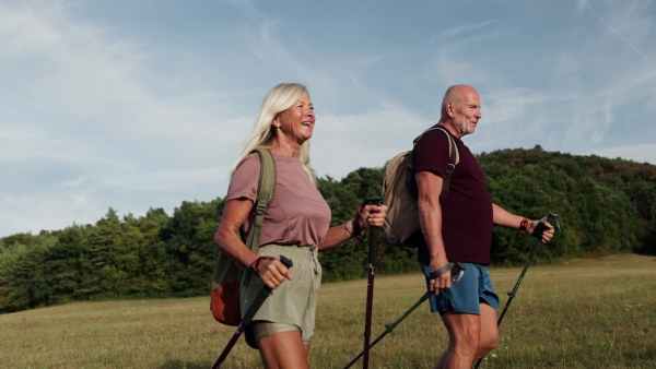 Active senior couple spending their free time outdoors, hiking in nature. Senior man and woman with trekking poles and backpack.