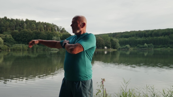 A video of senior man spending morning outdoors, exercising. Older man running by lake, checking his performance on smartwatch.