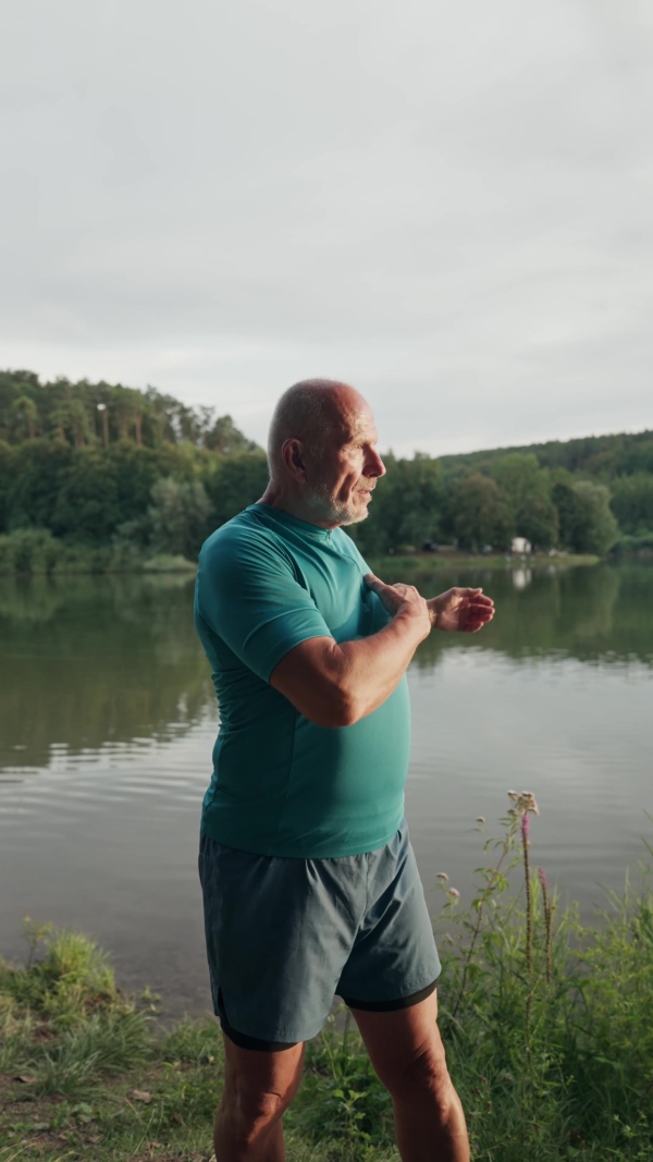 A video of senior man spending morning outdoors, exercising. Older man running by lake, checking his performance on smartwatch.