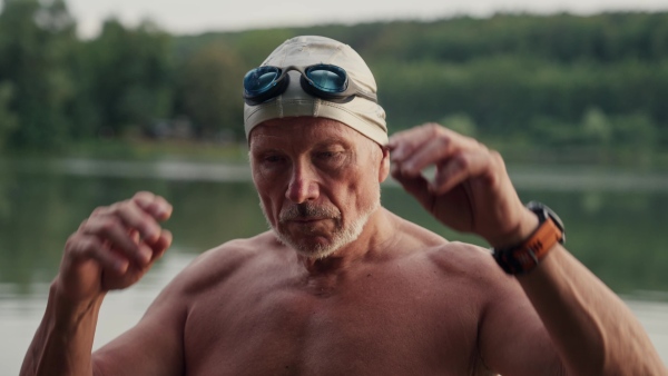 A senior man has a shared hobby, swimming in lake during cold autumn morning. Getting ready before going into water.