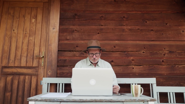 A senior man sitting outdoor on terrace, shopping online on notebook. Man holding debit card in hand, imputing card detail for payment.