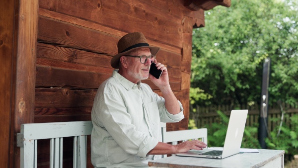 A senior man sitting outdoor on terrace, shopping online on notebook. Man holding debit card in hand, imputing card detail for payment.