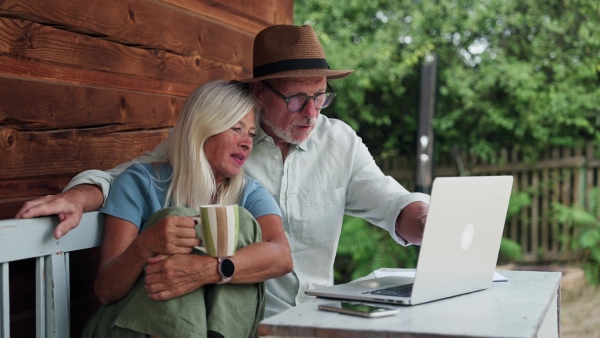 An elderly woman sitting beside her senior husband who is working on laptop.