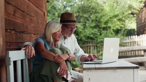 An elderly woman sitting beside her senior husband who is working on laptop.