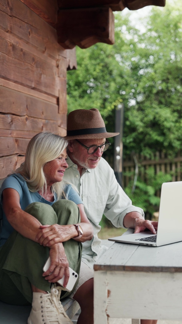 An elderly woman sitting beside her senior husband who is working on laptop.