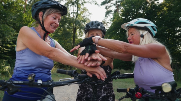 Three senior friends on their bike tour in nature, preparing for successful ride. Older women on low impact route riding electric bikes.