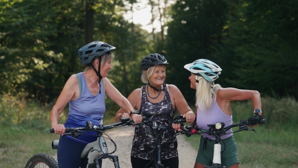 Three senior friends on their bike tour in nature resting. Older women on low impact route riding electric bikes.