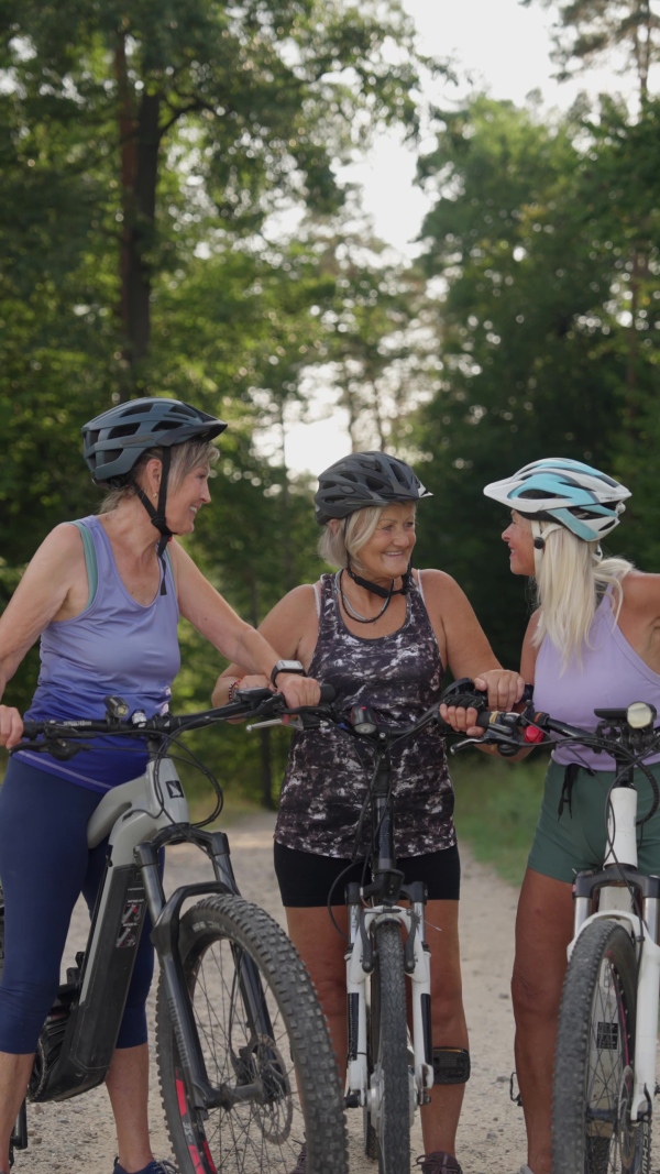 Three senior friends on their bike tour in nature resting. Older women on low impact route riding electric bikes.