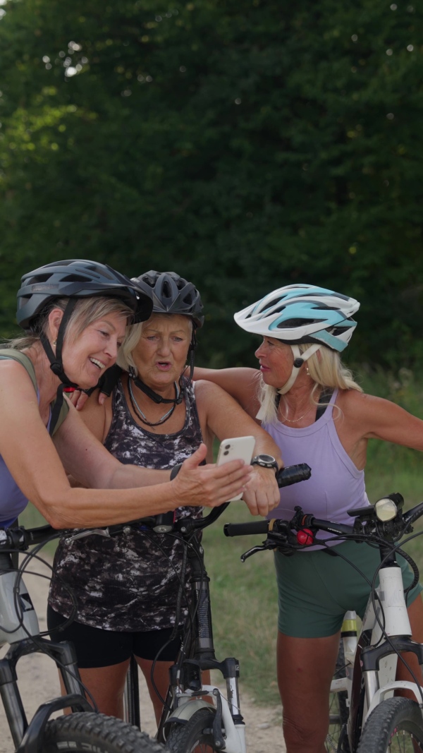 Three senior friends on bike tour in nature taking selfie. Older women on low impact route riding electric bikes.