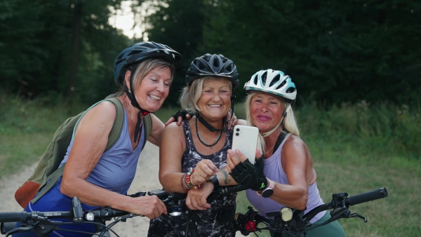 Three senior friends on bike tour in nature taking selfie. Older women on low impact route riding electric bikes.