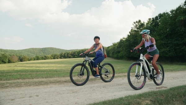 Three senior friends on their bike tour in nature enjoying ride. Older women on low impact route riding electric bikes.