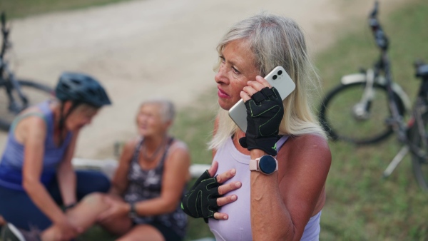 Senior cyclist fell off bike, injuring her knee. Elderly friends helping her, calling ambulance.