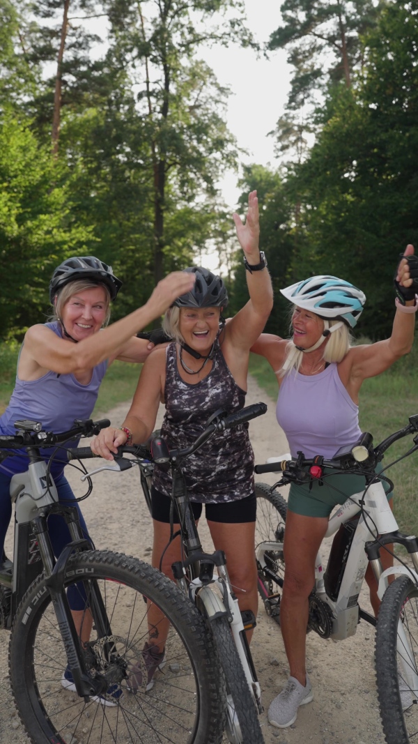 Three senior friends on their bike tour in nature resting, celebrating successful ride. Older women on low impact route riding electric bikes.